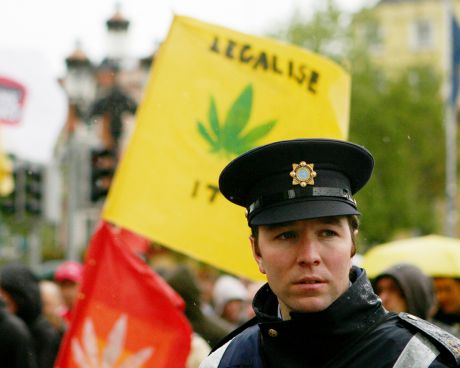 A member of the Garda Siochana stands in front of a Legalise It flag